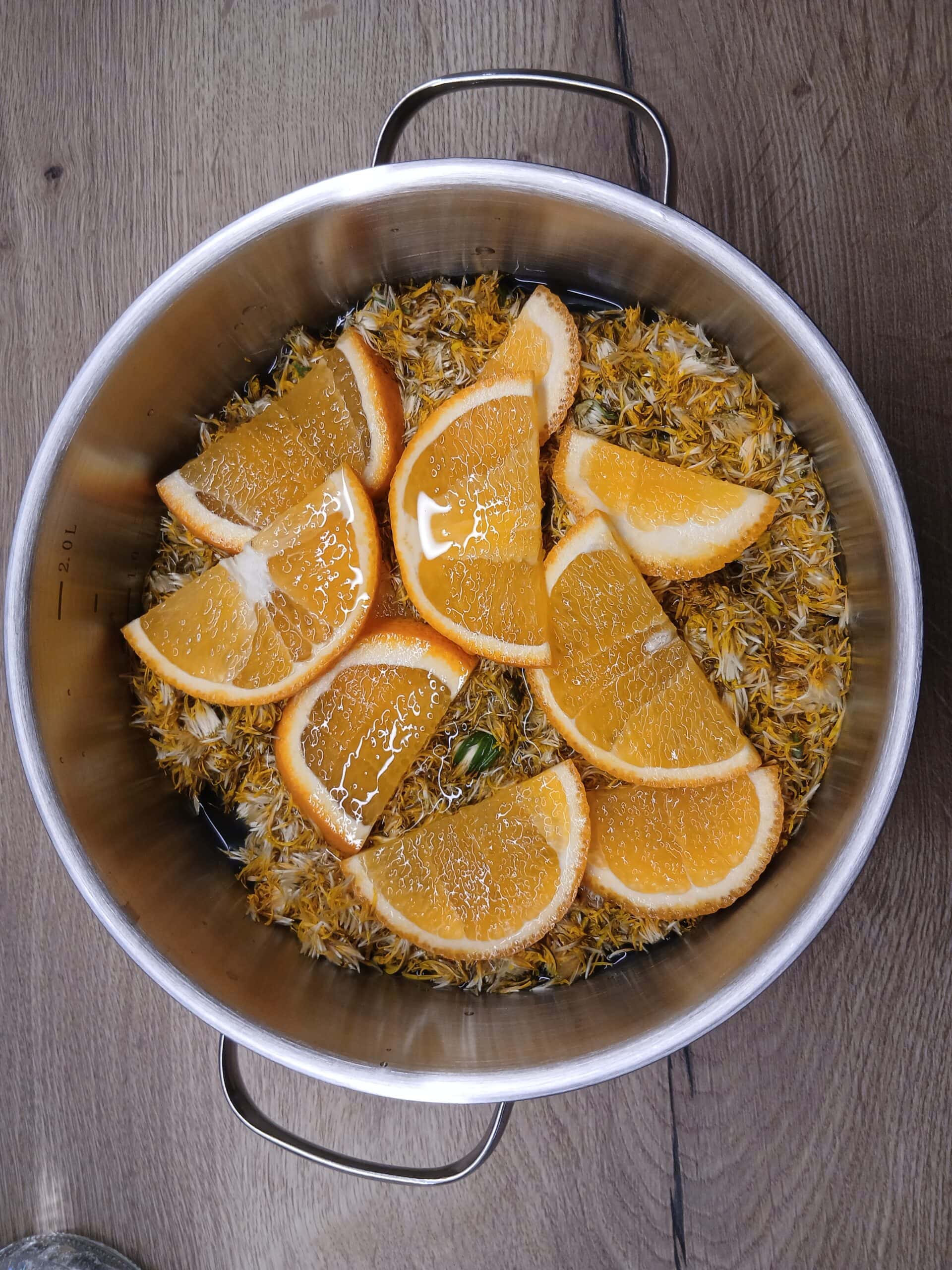 Löwenzahnblüten, Wasser und Orangenscheiben in einem Topf