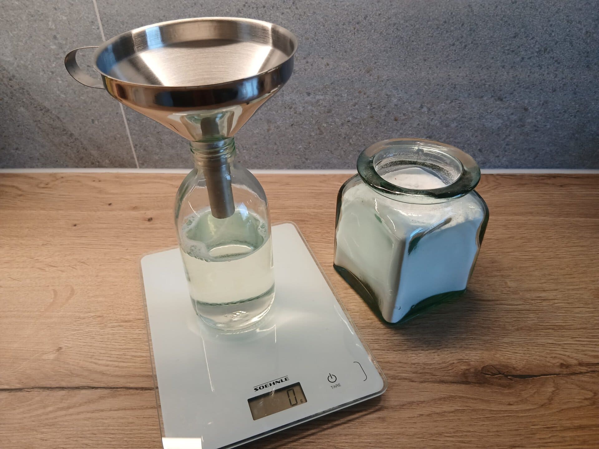 Eine Glasflasche mit Trichter auf einer Küchenwaage, neben einem Glas Waschsoda